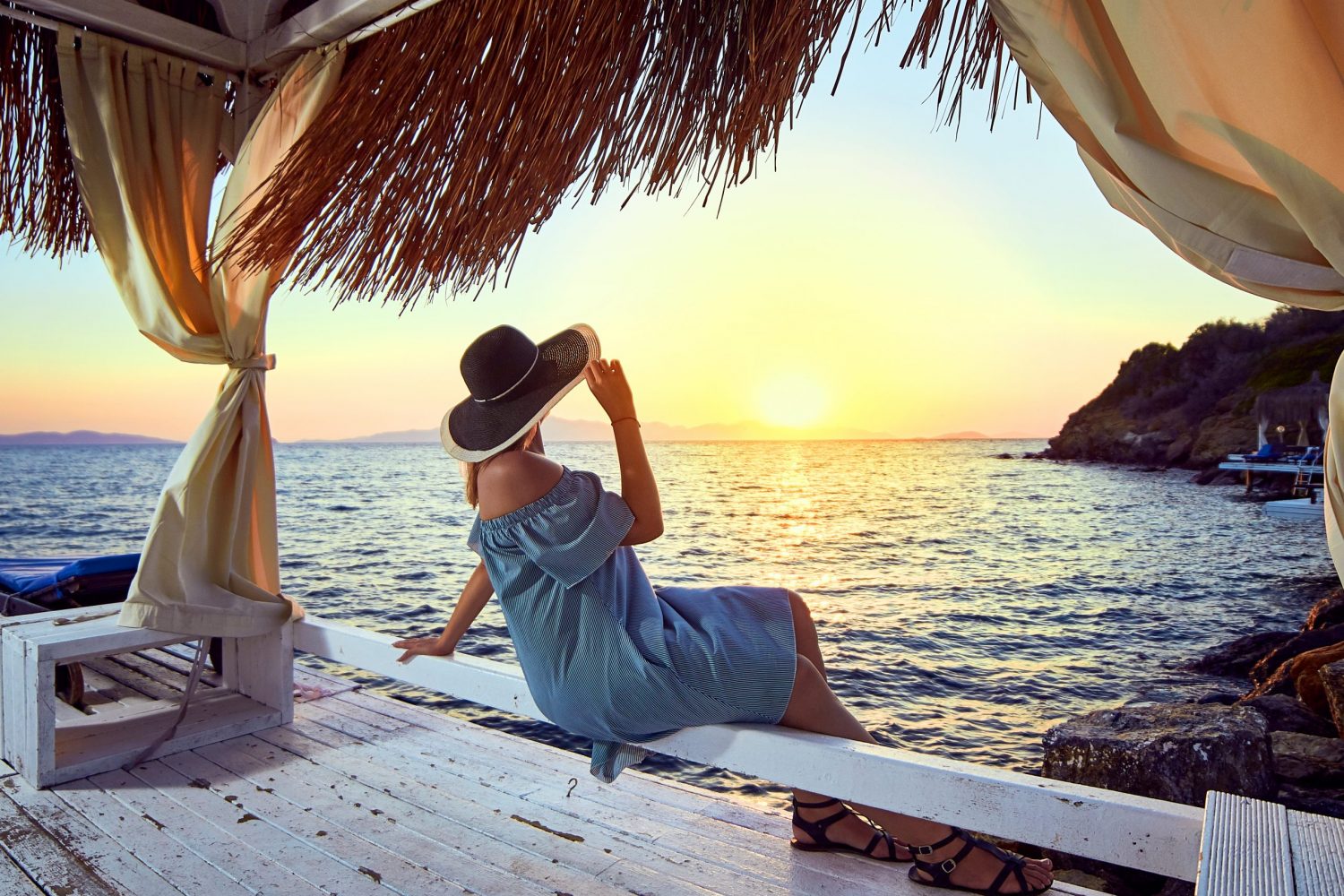 Woman in hat relaxing by the sea in a luxurious beachfront hotel resort at sunset enjoying perfect beach holiday vacation in Bodrum, Turkey. Outdoors Seascape Summer Travel Concept